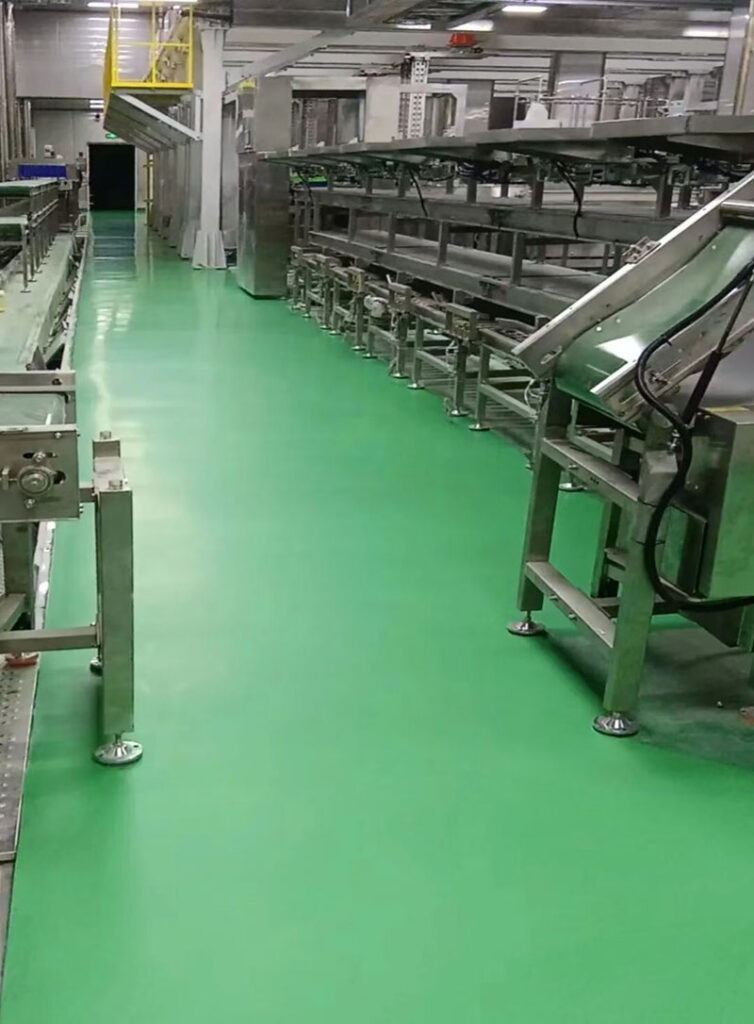 A wide shot of a finished seafood processing plant featuring a seamless, light green KAIDA JINYU urethane mortar floor with integrated coving and drainage, showcasing a clean and hygienic environment.