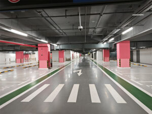 Shiny polyurethane-coated floor in a clean, empty underground car park with marked lanes, pink pillars, and overhead lighting