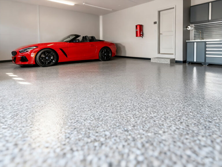 Durable polyaspartic garage flooring: high-gloss, stain-resistant, and chip-resistant flake surface, showcased in a residential garage with a red convertible—featuring long-lasting wear resistance and reflective sheen