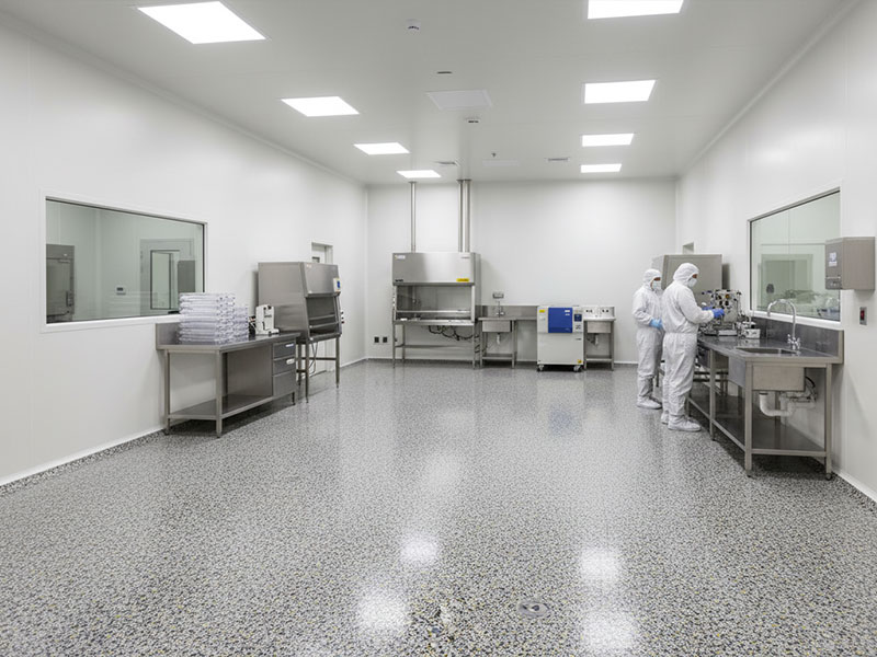 A sterile laboratory environment showcasing a four-layer decorative flooring system with a speckled quartz aggregate and vinyl flake finish in shades of grey and black.