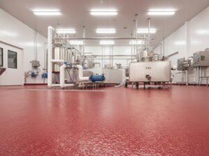 A clean industrial dairy processing plant featuring a textured red seamless floor coating and stainless steel machinery for hygienic food production.