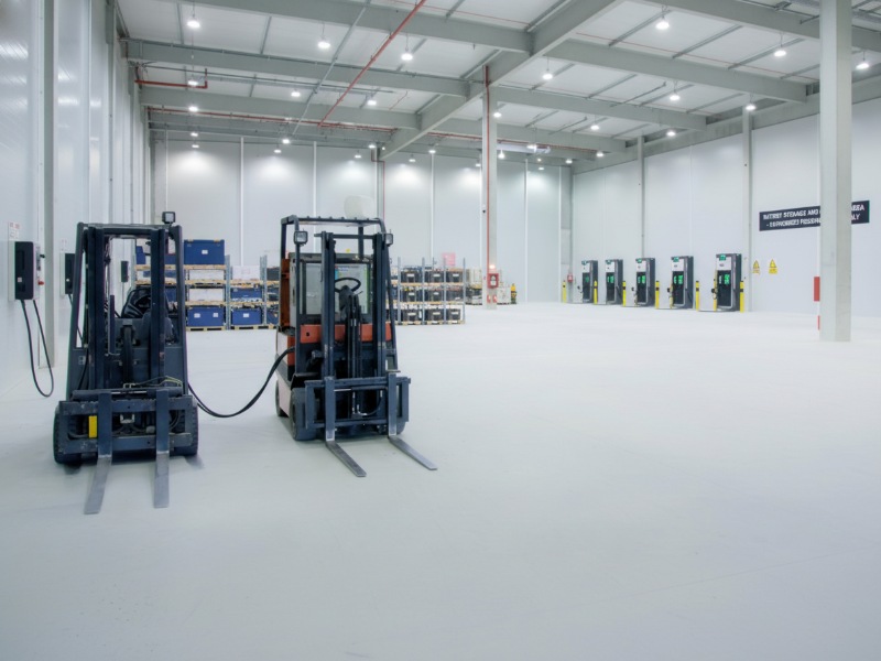 Electric forklifts charging on a durable, white, chemical-resistant KAIDA PAINT floor in an industrial warehouse battery storage area.