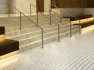 A modern commercial lobby featuring KAIDA PAINT's seamless and slip-resistant flooring system with a patterned tile design, elegant marble stairs, and stainless steel handrails.