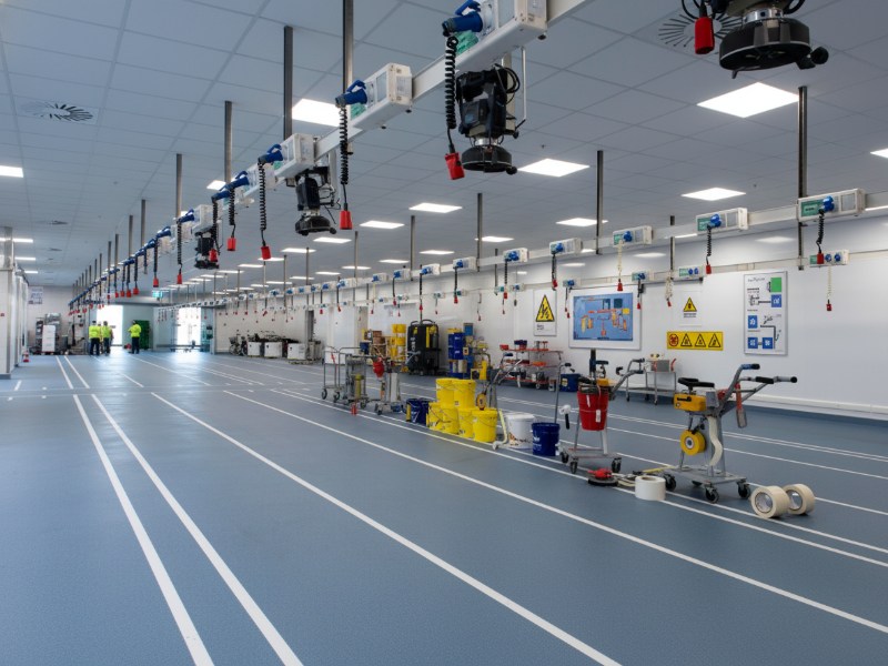 A large industrial manufacturing facility featuring bright blue flooring with professional white KAIDA PAINT floor striping and marking lines for enhanced safety and organizational efficiency.