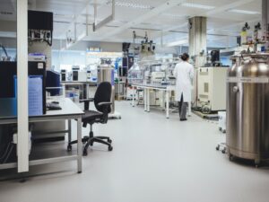 A clean and seamless KAIDA PAINT chemical-resistant laboratory flooring system in a pharmaceutical research lab with a scientist and heavy equipment.