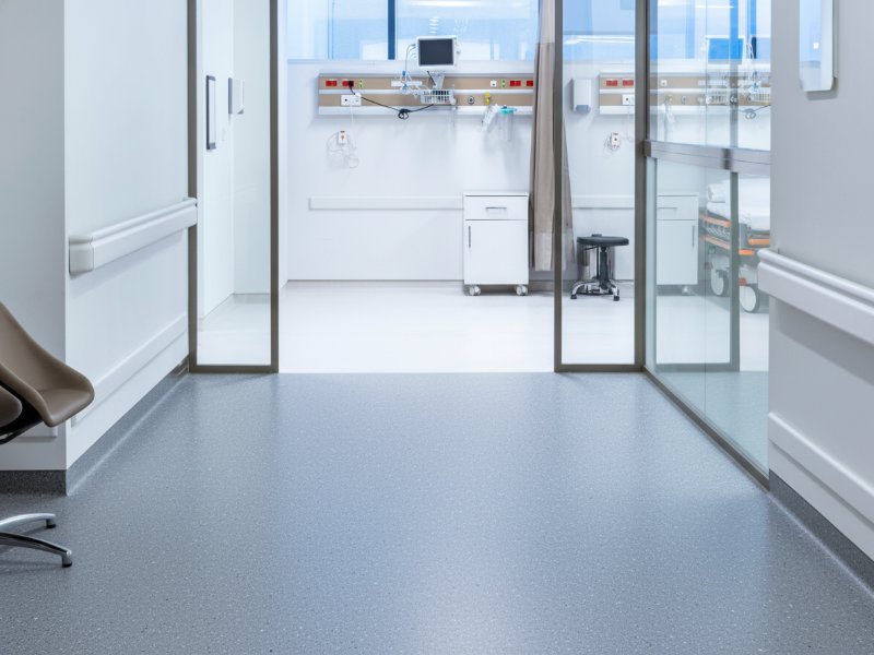 Durable grey seamless exam room flooring installed in a clean hospital corridor for superior hygiene and safety.
