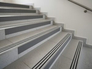 Durable KAIDA PAINT anti-slip stairwell flooring system with speckled grey tiles and black safety traction strips for commercial and industrial heavy foot traffic.