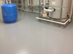 A durable and low-maintenance grey KAIDA PAINT epoxy flooring system installed in a mechanical room containing an expansion tank and water heater.