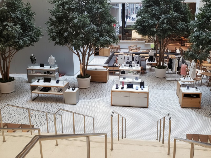 A modern, open-concept retail store featuring KAIDA PAINT's high-quality, seamless resinous flooring with a clean mosaic pattern, showcasing product display tables and indoor trees in a durable commercial shopping environment.