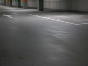 Seamless and slip-resistant grey KAIDA PAINT parking deck flooring installed in a clean commercial garage with white parking bay lines and directional arrows.