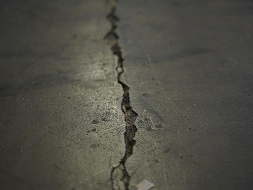 Macro shot of a deep structural crack in the concrete substrate at a Swedish factory, requiring epoxy mortar injection.