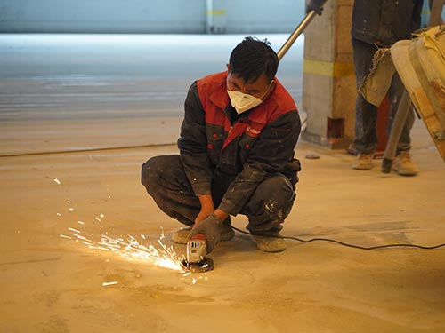 Hand-grinding concrete imperfections to ensure a flat and stable base for epoxy flooring in a Swedish factory.