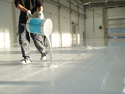Detailed view of worker pouring white epoxy resin during the 27-day rapid factory renovation in Sweden.