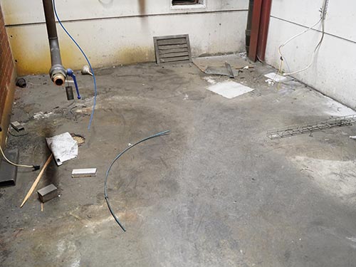 Corner of a Swedish industrial facility showing stained walls and debris-covered concrete before the integrated renovation.