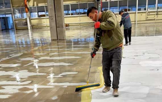 Worker applying epoxy primer during concrete floor renovation at a Hungary battery manufacturing facility