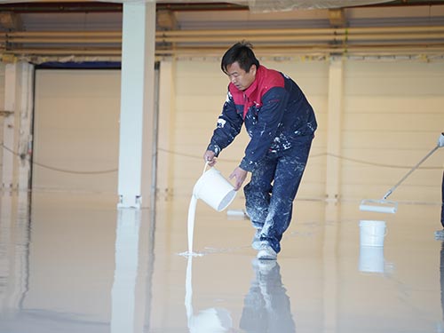 Applying the white self-leveling epoxy coating layer on a Swedish factory floor during the rapid renovation process.