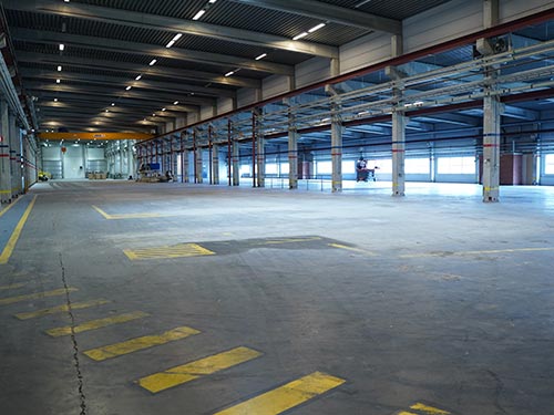 Wide perspective of the aging industrial floor at a Swedish manufacturing plant showing yellow safety markings and worn concrete.