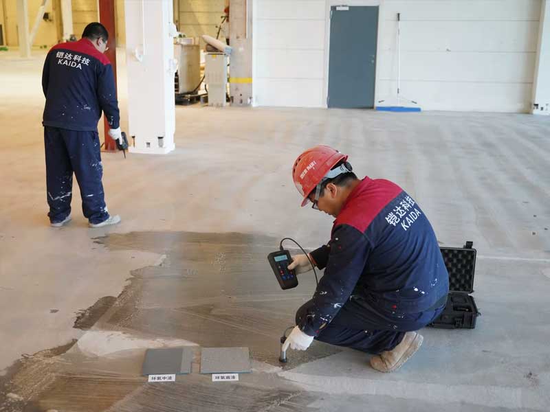 Technical specialist in a KAIDA Technology uniform using a moisture meter to test the concrete substrate, demonstrating professional pre-treatment and engineering expertise before flooring installation.