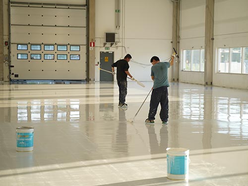 KAIDA flooring team using squeegees to distribute epoxy coating across a large industrial hall in Sweden.