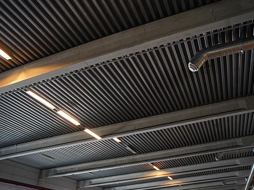 Interior view of the corrugated metal roof structure in a Swedish factory, showing the pre-renovation state of the ceiling.