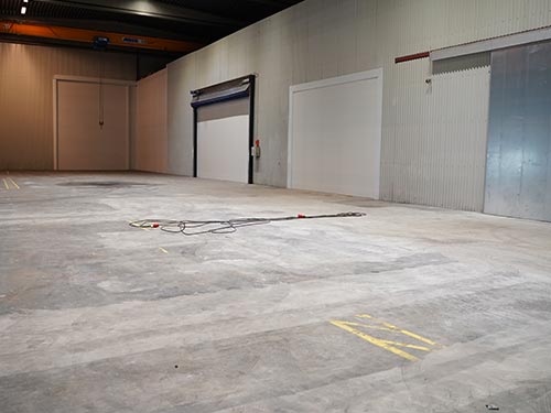 Worn-out concrete surface near the loading bay of a Swedish plant, showing severe mechanical wear and unevenness.