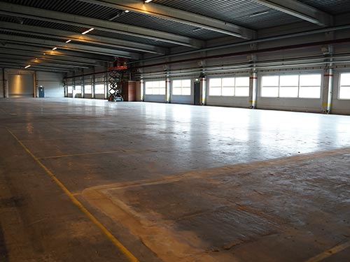Wide perspective of the aging industrial floor at a Swedish manufacturing plant showing yellow safety markings and worn concrete.