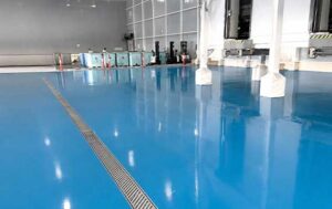 Completed high-gloss blue polyurethane mortar flooring with a stainless steel linear drain in a Maracaibo seafood processing plant.