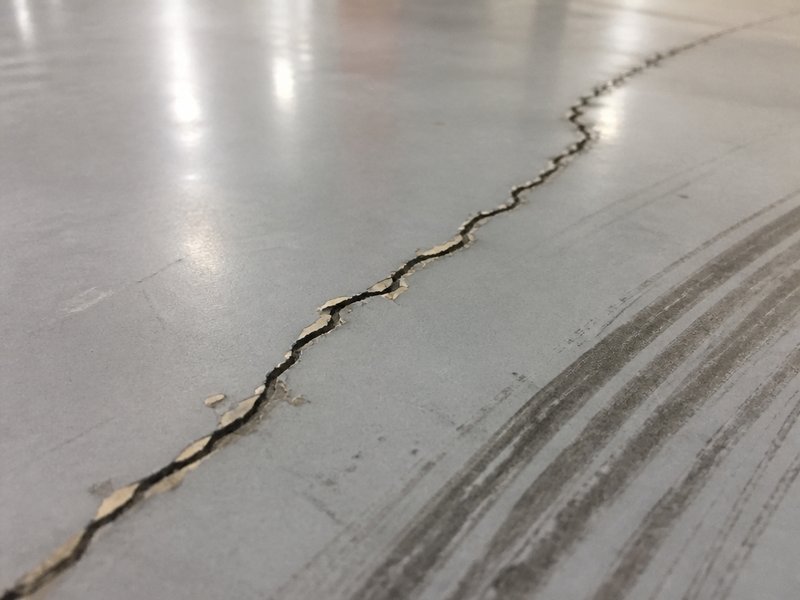 A concrete crack reflecting through the epoxy film, causing a visible fault line and peeling film