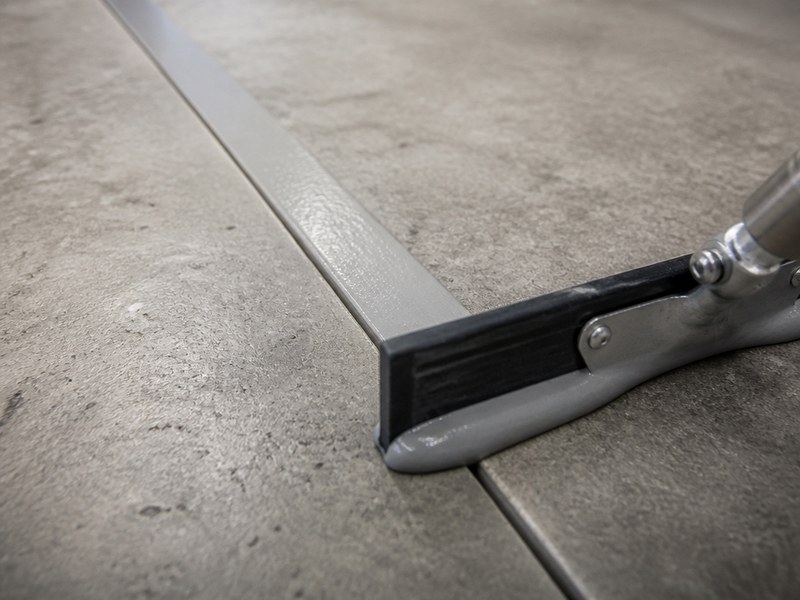 Filling a chased concrete control joint flush with semi-rigid urethane cement joint filler before the self-leveling urethane cement topping is poured