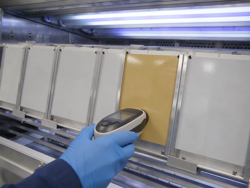 Epoxy floor topcoat samples inside a QUV accelerated weathering chamber, showing one yellowed aromatic epoxy sample beside an unchanged polyaspartic sample