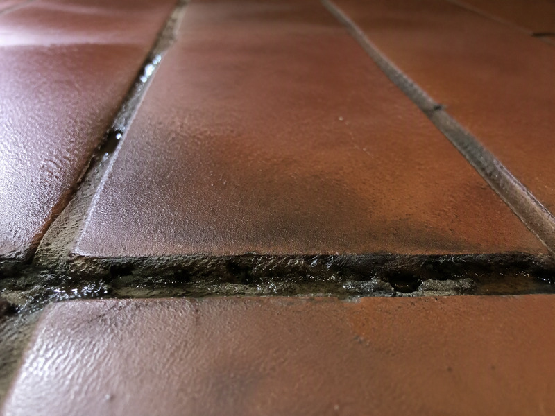Close-up of eroded grout joints between quarry tiles in a commercial kitchen with grease staining along the joint lines